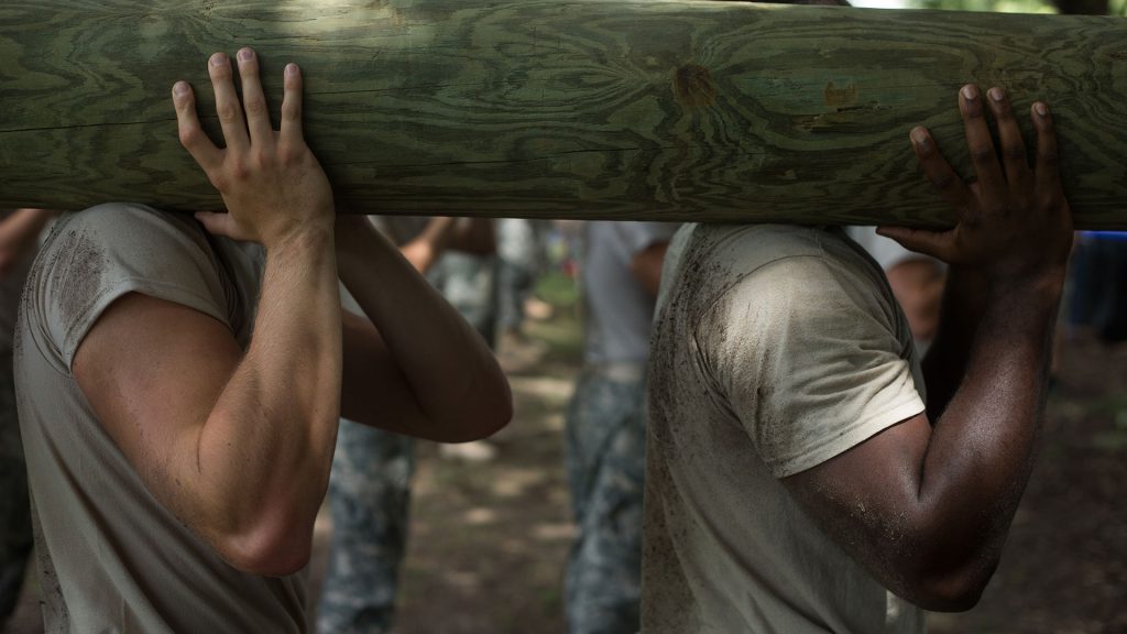 Two men carry a log over their shoulder