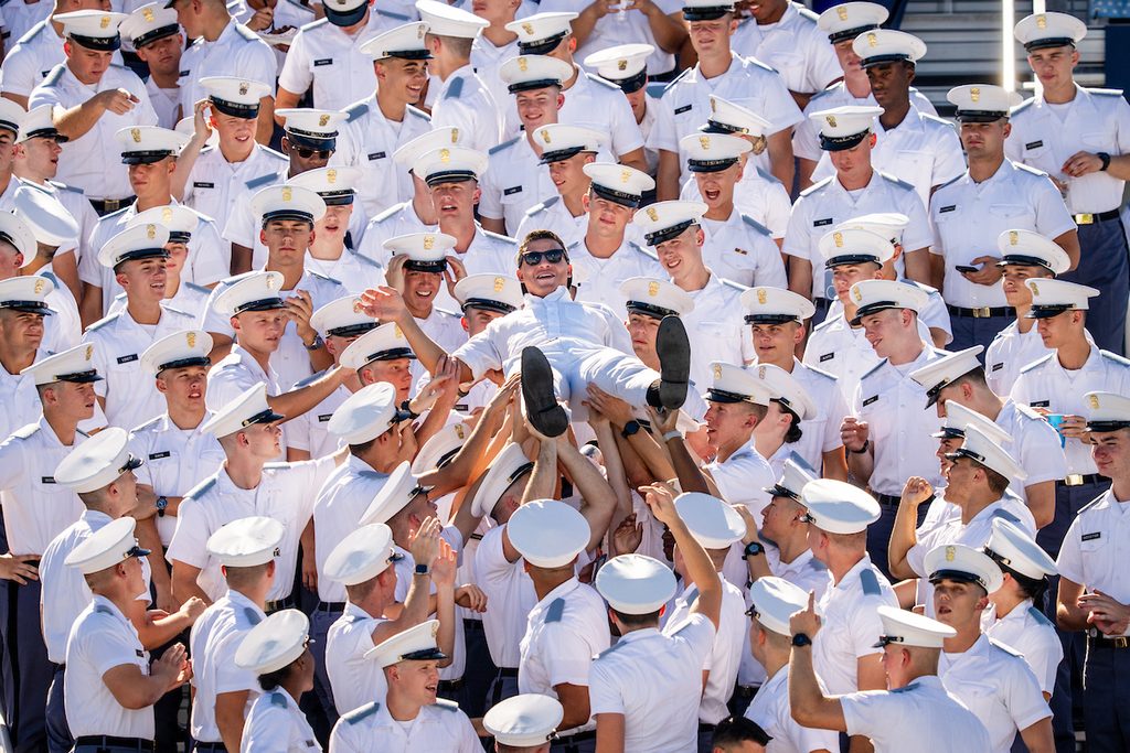 A group of uniformed personnel joyfully lifts one member into the air in a celebratory moment.