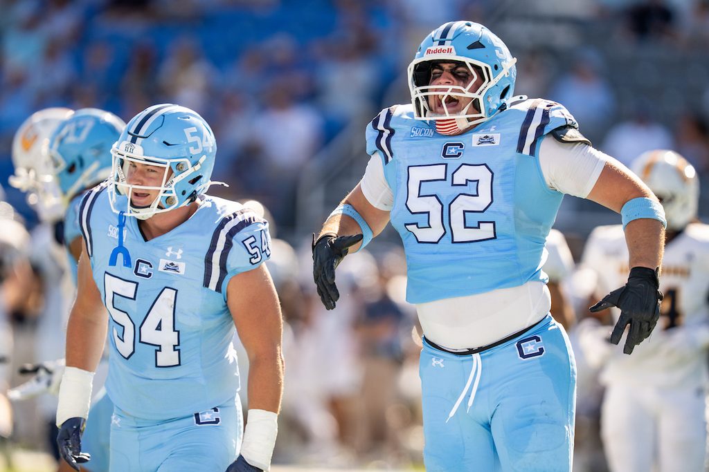 Two football players in light blue uniforms with numbers 52 and 54 celebrate on the field during a game.