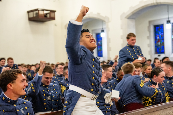 A cadet in uniform raises a fist in celebration while others around him share in the moment during a formal gathering.