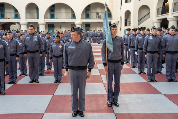 Uniformed personnel stand in formation on a checkered courtyard during a formal event.