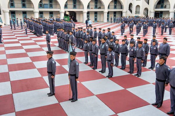 Uniformed personnel stand in precise formation on a red and white checkered courtyard during a formal ceremony.