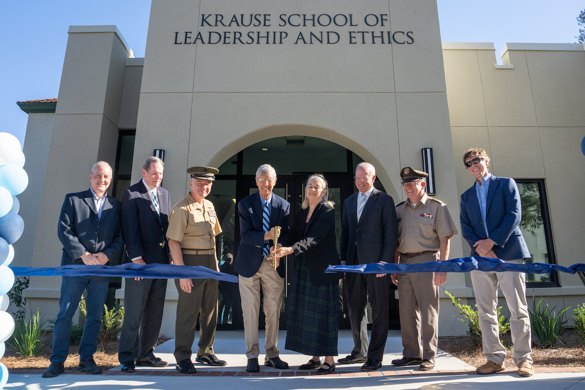 A group of individuals, including uniformed personnel and civilians, stands in front of the Krause School of Leadership and Ethics for a ribbon-cutting ceremony.